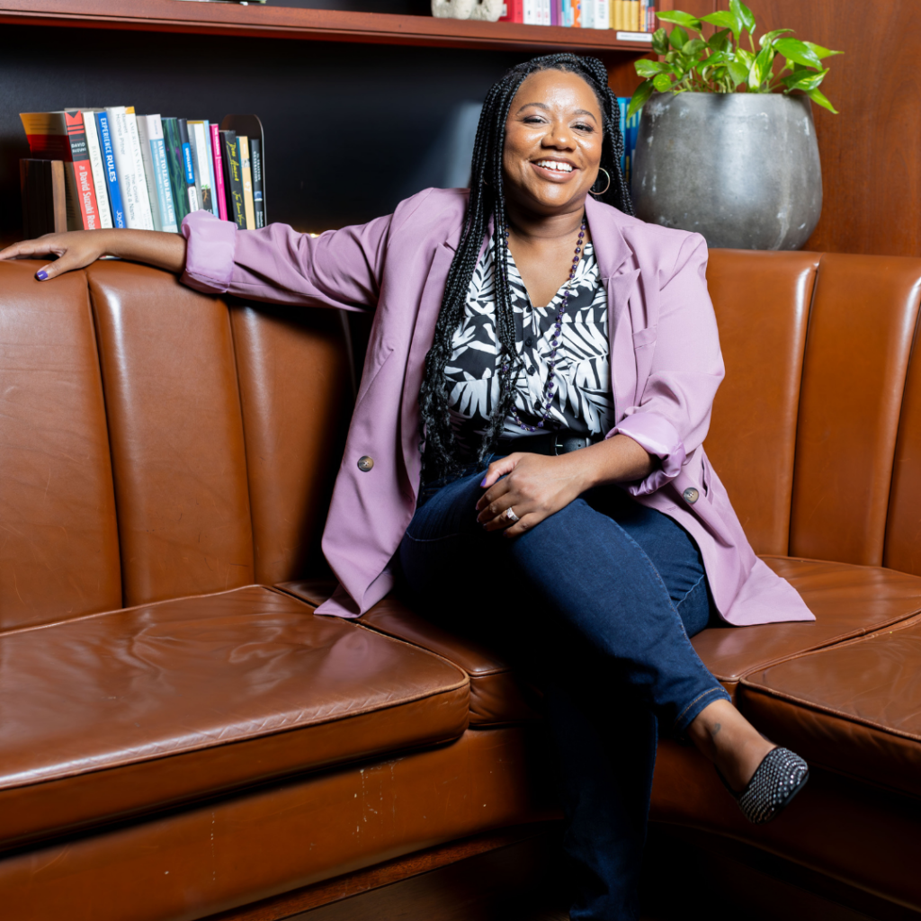 Photo of author, keynote speaker, and founder Ashley Cuthbertson sitting casually on a leather couch smiling.